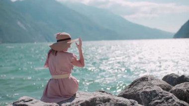 Neşeli bir kadın kıyıya yakın arka planda çarpıcı bir deniz manzarası olan kayaların üzerinde oturur. Güzel deniz manzarası.