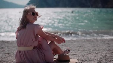 Neşeli bir kadın okyanus, mavi su ve dağ zeminiyle gün ışığında gülümsüyor..