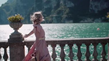 Denizin derinliklerine bakan bir kadın sahil yolu boyunca yürüyor. Huzurlu sahil atmosferini yakalar.