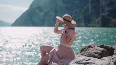 Şapka takan ve güneş gözlüğü tutan neşeli bir kadın güzel bir kıyı manzarasının tadını çıkarıyor..
