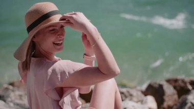 Elinde hasır şapka tutan gülümseyen bir kadının, çarpıcı bir mavi deniz geçmişine yakın çekimi..