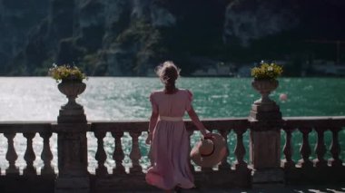 Kadın beton bariyerlere yaklaşıyor, denize bakıyor, açık bir günde güzel deniz manzarasına hayran..