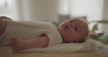 Sevimli erkek bebek, tatlı tatlı gülümserken kollarını ve bacaklarını oynatıyor. Mutlulukla dolu hassas bir anı yakalar.