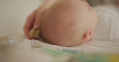 Bir bebeğin başını nazikçe yakın plan çekerken annesi saçlarını tarar ve kafa derisine bakar. Şefkat ve özen gösterir..