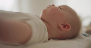 Sevimli erkek bebek masasını değiştiriyor, düşünceli bir ifadeyle kameraya gülümsüyor..