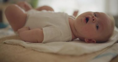 Mutlu ve meraklı bir çocuk değişen bir masada uzanıyor, hareket ediyor ve oynuyor, etrafındakileri dikkatle izliyor..