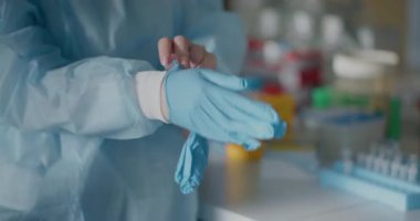 A female scientist in a medical lab puts on protective gloves before conducting experiments.
