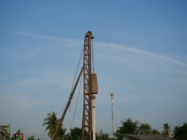 İnşaat alanındaki beton yığını mavi gökyüzü ve beyaz bulutlu sütun makinesi kullanılarak yere dökülüyor. Diesel çekiç yığını sürüş makinesi çalışıyor. 