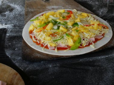 Ananas ve tatlı ile mozzarella peynirli jambon dilimleri veya domates soslu dolmalık biber ve tahta tepside düz yuvarlak pizza hamuru.