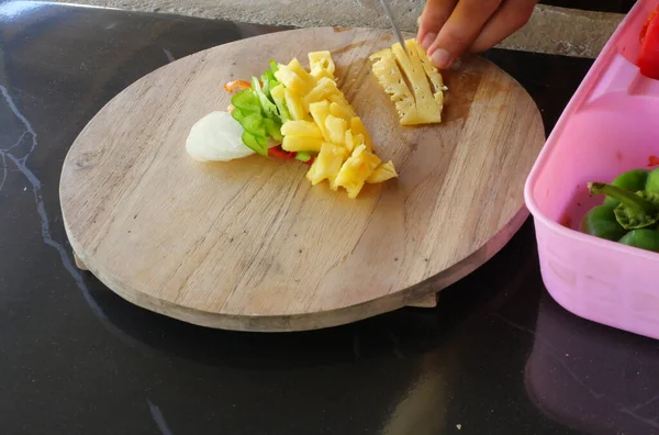 シェフはピーマンとパイナップルの果物を木製のまな板にナイフでスライスしています — ストック写真