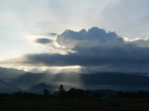 stock image Silhouette of tree and mountain with sunbeam light shoot through the dark cloud to the land at sunrise, Mist covers the forest and mountains at dawn at Pua District, Nan Province, Thailand