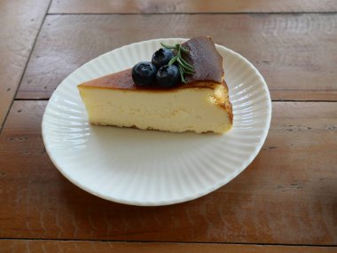 Üstünde yaban mersini meyvesi olan cheesecake pastası dilimi arka planda kahverengi masa olan tatlı yemek.
