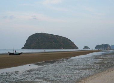 Koh Nom Sao Adası Khao Sam Roi Yot Milli Parkı 'nda, balıkçı teknesi denizde yüzüyor kumsalda kahverengi kum ve arka planda mavi gökyüzü, Tayland