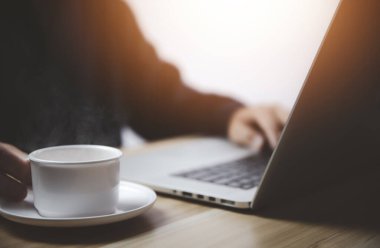 İş adamı laptopun önünde çalışıyor. Elinde dumanı ve buharı olan bir fincan sıcak kahveyle.