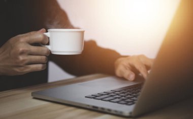 İş adamı laptopun önünde çalışıyor. Elinde dumanı ve buharı olan bir fincan sıcak kahveyle.