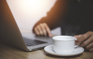 İş adamı laptopun önünde çalışıyor. Elinde dumanı ve buharı olan bir fincan sıcak kahveyle.