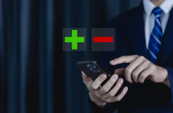 Businessman using smartphones show plus and minus signs. Concept of opposites, decisions, and uncertainty. Positive or Negative Business Choices Analysis of advantages and disadvantages Comparison