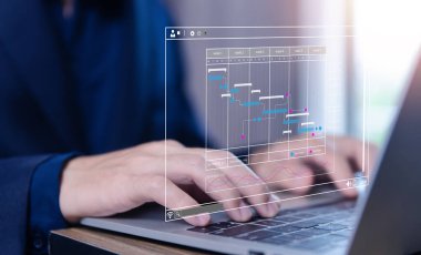 Ofisteki iş planlama programını yöneten erkek yönetici. Gantt grafiği sanal ekranda görünüyor. İş adamları internetteki dijital teknolojide bilgisayar verilerini yönetirler