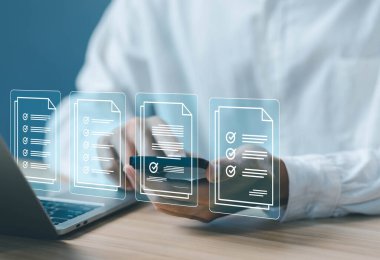 Biri telefonundaki ve laptopundaki işaretleri işaretliyor. Belgeler listesinde, denetim kontrol formu çevrimiçi. İş konsepti görev ayrıntısını ve değerlendirme işaretini, kontrol listesi işlem sırasını doğrula.