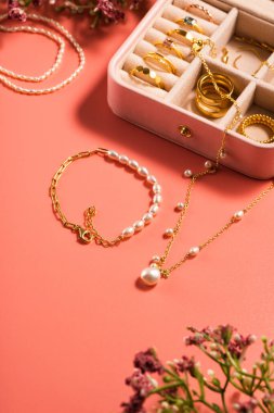 Zarif altın yüzüklü mücevher kutusu, küpeler, pembe arka planda inci bilezikler.