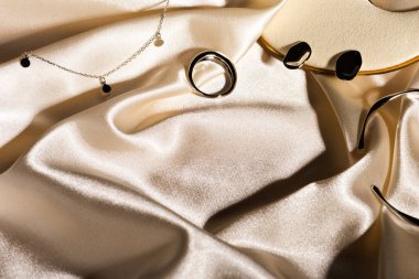 Şık gümüş yüzük, küpeler, bej rengi ipek arka planda kolye. Metin için alanı kopyala