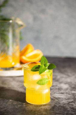 Limonata veya meyve ve fesleğenli mojito kokteyli. Limonlu ve portakallı soğuk yaz içeceği gri masada.