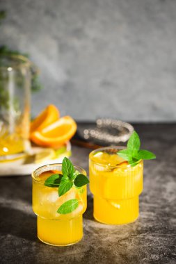 Limonata veya meyve ve fesleğenli mojito kokteyli. Limonlu ve portakallı soğuk yaz içeceği gri masada.