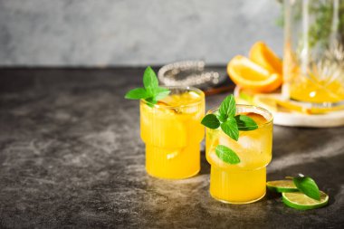 Limonata veya meyve ve fesleğenli mojito kokteyli. Limonlu ve portakallı soğuk yaz içeceği gri masada.