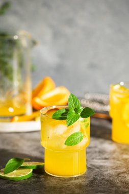 Limonata veya meyve ve fesleğenli mojito kokteyli. Limonlu ve portakallı soğuk yaz içeceği gri masada.