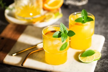 Limonata veya meyve ve fesleğenli mojito kokteyli. Limonlu ve portakallı soğuk yaz içeceği gri masada.