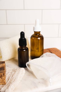 Sürdürülebilir sıfır atık yaşam tarzı serum şişeleri ve beyaz fayanslı banyo aksesuarları. Metnin için boşluk kopyala
