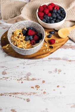 Bir kase ev yapımı yulaf gevreği yoğurt ve ahşap bir masada taze böğürtlen. Ceviz ve kuru üzümlü sağlıklı bir kahvaltı.