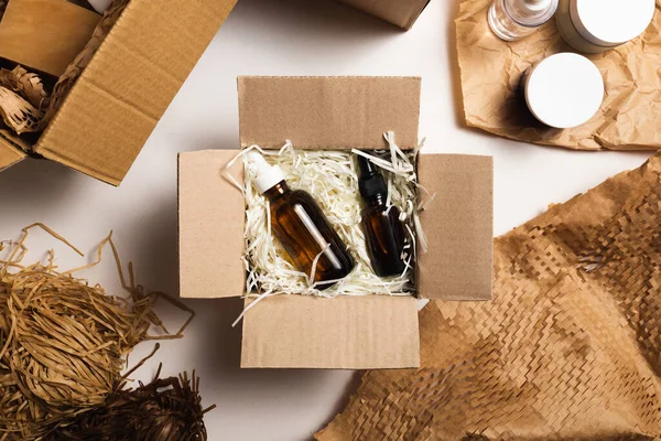 Beauty box with serum bottles on shredded white paper. Eco-friendly cardboard gift box with zero-waste cosmetics products. Online retail store orders in the delivery service warehouse.
