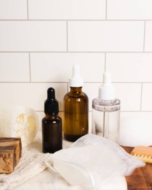 Sürdürülebilir sıfır atık yaşam tarzı serum şişeleri ve beyaz fayanslı banyo aksesuarları. Metnin için boşluk kopyala