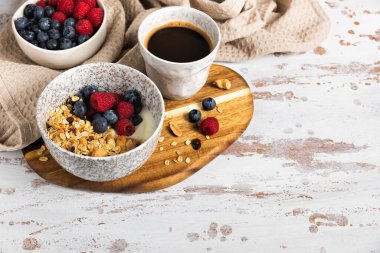 Bir kase ev yapımı yulaf gevreği yoğurt ve ahşap bir masada taze böğürtlen. Ceviz ve kuru üzümlü sağlıklı bir kahvaltı.