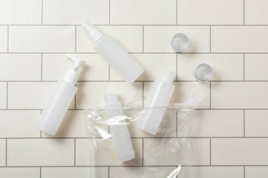 Beyaz banyo fayanslarının üzerinde kozmetik seyahat seti olan plastik torba. Seyahat için el bagajı. Yüze, vücuda ve saçlara güzellik seti. Plastik bir çantada.