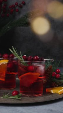 Buzlu ve biberiyeli yabanmersinli Noel kokteyli. Portakal, böğürtlen, tarçın ve anasonlu baharatlı içecek. Dikey video