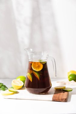 Bardak bardaklar, bir sürahi limon ve limonlu buzlu çay beyaz bir masada. Güneşli bir gün ve keskin gölgeler limonata bardağından