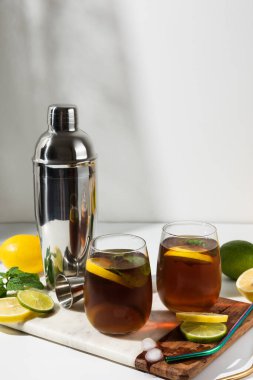 Bardak bardaklar, bir sürahi limon ve limonlu buzlu çay beyaz bir masada. Güneşli bir gün ve keskin gölgeler limonata bardağından