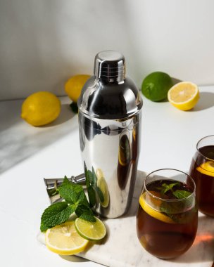 Bardak bardaklar, bir sürahi limon ve limonlu buzlu çay beyaz bir masada. Güneşli bir gün ve keskin gölgeler limonata bardağından