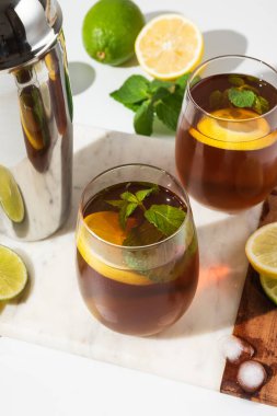 Bardak bardaklar, bir sürahi limon ve limonlu buzlu çay beyaz bir masada. Güneşli bir gün ve keskin gölgeler limonata bardağından