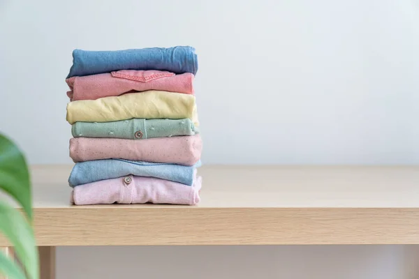 Stack of clean freshly laundered, neatly folded womens clothes on wooden table. Pile of shirts and sweaters on the table