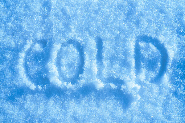 Слово "холодный" написано на снегу в солнечную погоду. Концепция зимней и холодной погоды.       