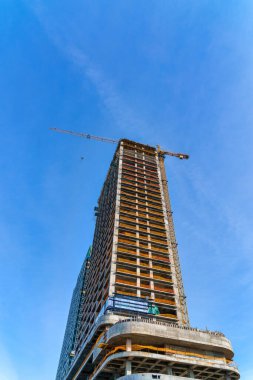 A crane building a modern skyscraper against a blue sky. Construction site.