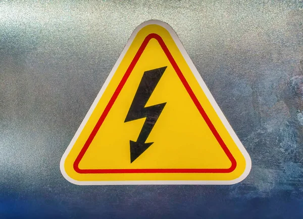 High voltage sign in the form of a lightning bolt on a yellow triangle on a metal surface.