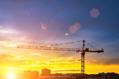 Elevating construction crane against the background of the sunset cloudy sky.