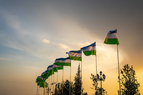 夕日や日の出に揺れるウズベキスタンの国旗劇的な曇天の背景 — ストック写真