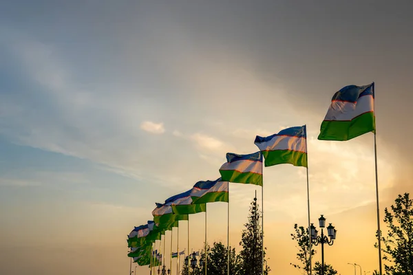 夕日や日の出に揺れるウズベキスタンの国旗劇的な曇天の背景 — ストック写真