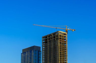 A crane building a modern skyscraper against a blue sky. Construction site.