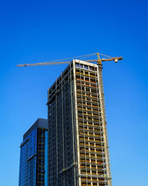 Een Kraan Die Een Moderne Wolkenkrabber Tegen Een Blauwe Lucht — Stockfoto